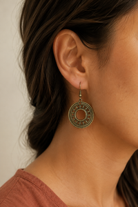 A close-up side profile of a woman wearing an ornate bronze circular drop earring with intricate filigree detailing.
