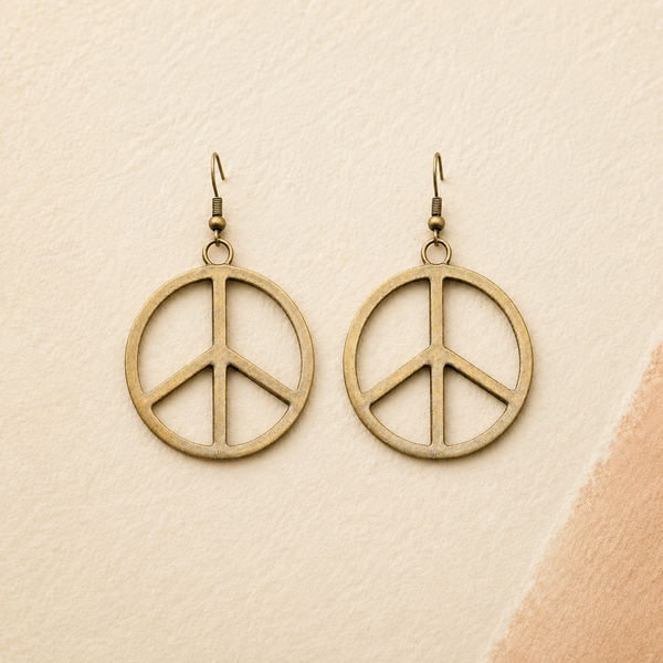 A pair of round peace sign dangle earrings in an antique bronze finish, displayed on a textured beige background with a soft peach-colored corner accent.